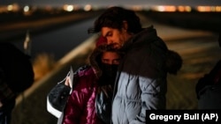 El migrante cubano Mario Pérez sostiene a su esposa mientras esperan ser procesados para solicitar asilo, luego de cruzar la frontera hacia EEUU, el 6 de enero de 2023, cerca de Yuma, Arizona. (AP/Gregory Bull)