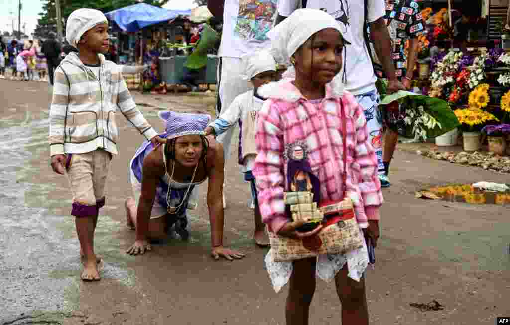 Una mujer junto a sus hijos camina de rodillas para pagar una promesa a San Lázaro, o Babalú Ayé, en el día del santo, en El Rincón, La Habana.