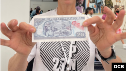 Coco Fusco muestra uno de los billetes marcados de la obra de Hamlet Lavastida.