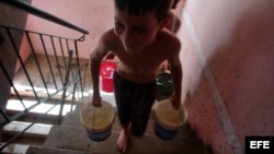 Un niño carga dos cubos de agua por las escaleras de su casa.