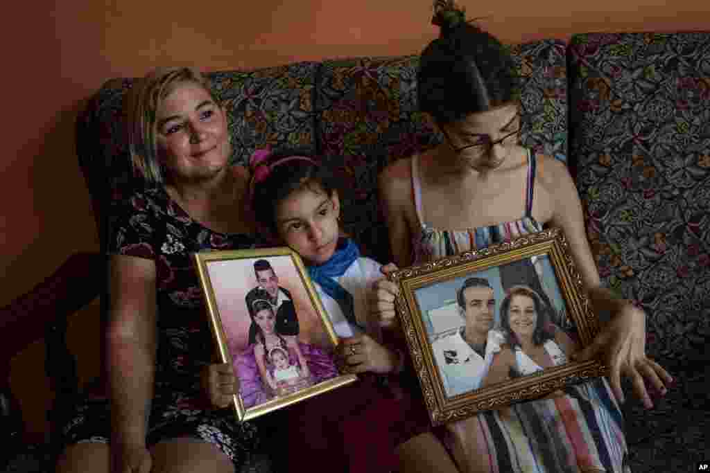 Danmara Triana (izquierda), con sus hijas Alice (centro) y Claudia, muestran fotos suyas con su hermano y su padres, quienes se mudaron a Estados Unidos en 2015.  (AP Foto/Ramón Espinosa)
