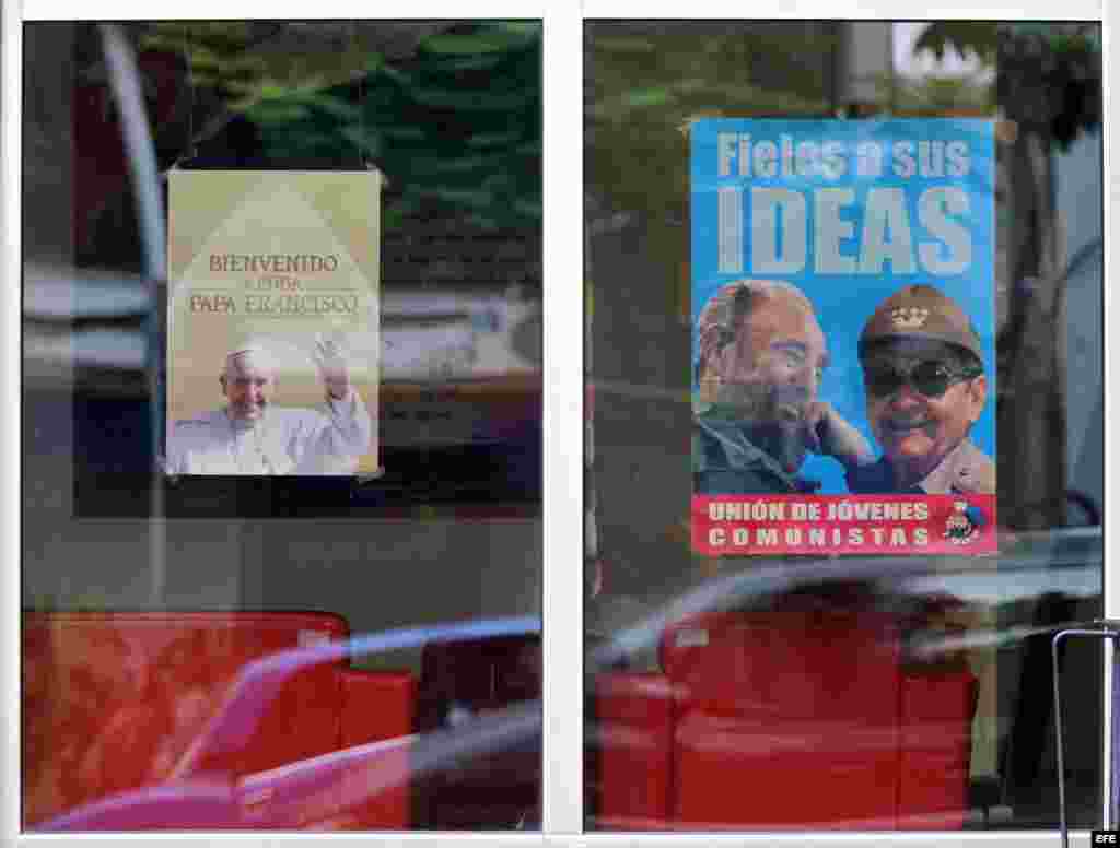 Vista de un cartel con la imagen del papa Francisco (i) junto a retratos de los hermanos Castro. EFE